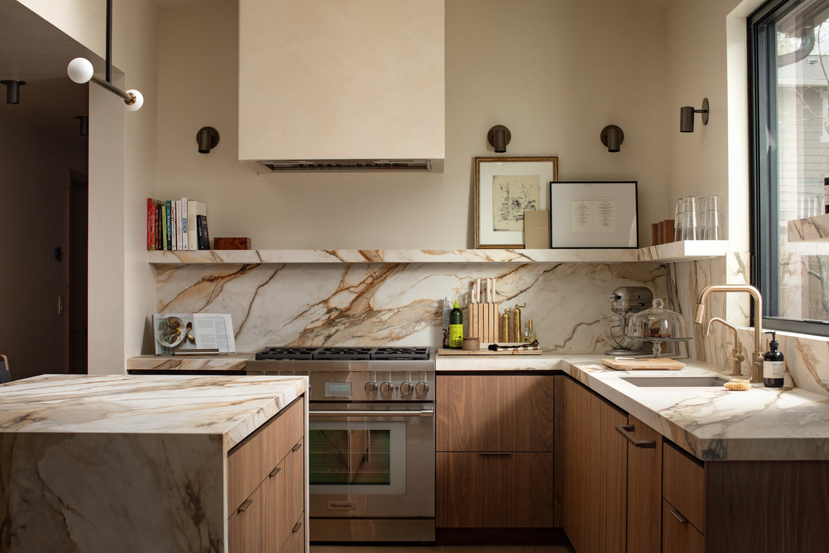 Modern kitchen with light wood cabinets, marble countertops and backsplash, gas stove with oven, open shelves, under-cabinet lighting, a large window for natural light, and Long Made Co.'s Brass Cylinder Adjustable Spot - Side Mount for stylish illumination.