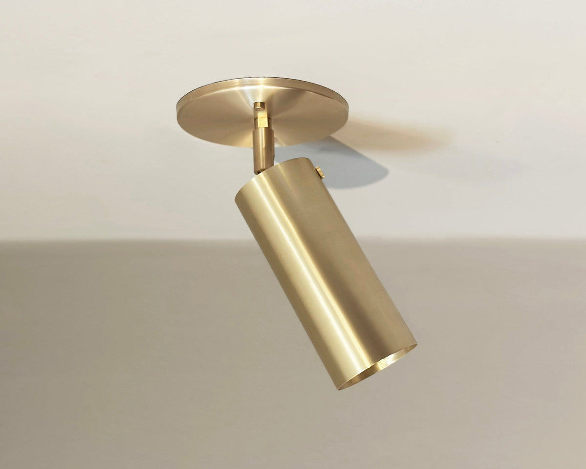 The Brass Cylinder Adjustable Spot - Top Mount w/ Long Shade by Long Made Co. features a modern cylindrical brass design on a round base, offering sleek, mid-century inspired directional lighting for any room.