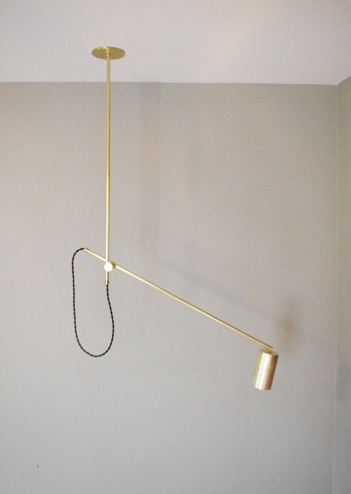 The Task Articulating Chandelier by Long Made Co. is a handmade brass ceiling light with an adjustable arm and black cord, blending modern design and UL-certified safety for versatile task lighting against any décor.