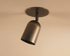 The Campana Adjustable Spot by Long Made Co. is a modern brushed metal ceiling downlight with a cylindrical shade on a circular base, angled downward against a light-colored ceiling.
