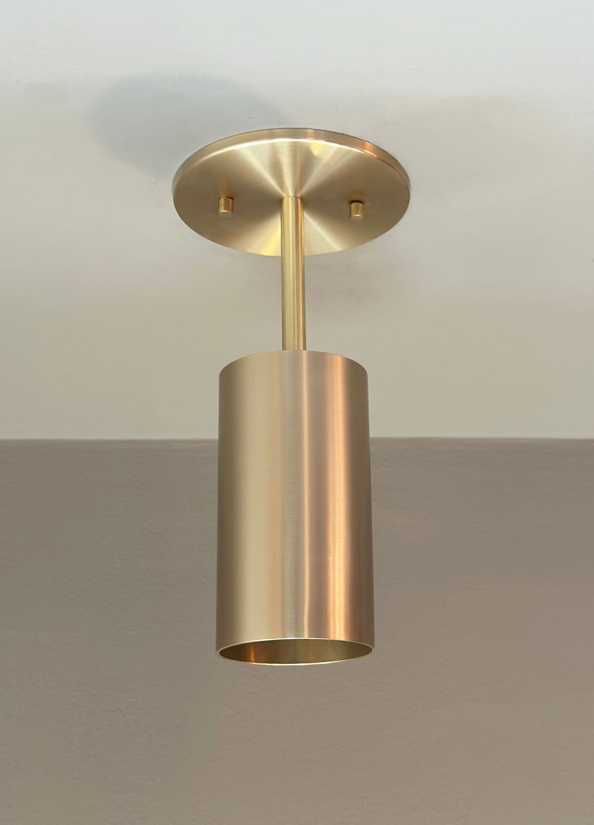 The Highland Drop Spot by Long Made Co. is a brass ceiling mono point fixture with a cylindrical shade and round base, flush-mounted for sleek, minimalist task lighting in any contemporary space.