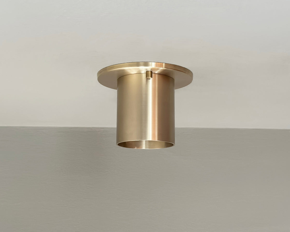The Highland Flush Spot - Stocky by Long Made Co. is a modern solid brass cylinder light with a round base, flush monopoint design, and is mounted on a smooth white ceiling.