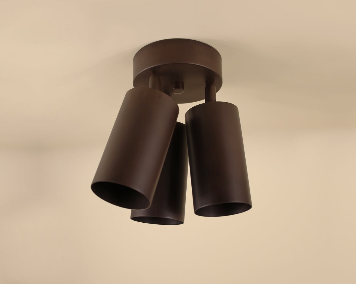 The Long Made Co. Cove Triple Spot features three cylindrical dark brown metal shades, angled downward from the ceiling, bringing minimalist style and modern design to any space.