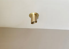 The Highland Angle Spot - Stocky by Long Made Co. is a modern solid brass flush ceiling fixture with a minimalist cylinder shape, mounted on a white ceiling above a beige wall for general and task lighting.
