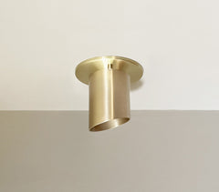 The Highland Angle Spot - Stocky by Long Made Co. is a modern, solid brass flush ceiling fixture, mounted above a beige wall, delivering general and task lighting with its minimalist cylinder design.