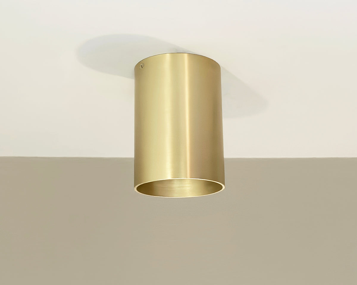 The Beau Laiton Trimless Downlight by Long Made Co. is a cylindrical brass fixture with a smooth, metallic finish and open bottom, mounted on a white ceiling to cast soft shadows and bring understated elegance to any space.