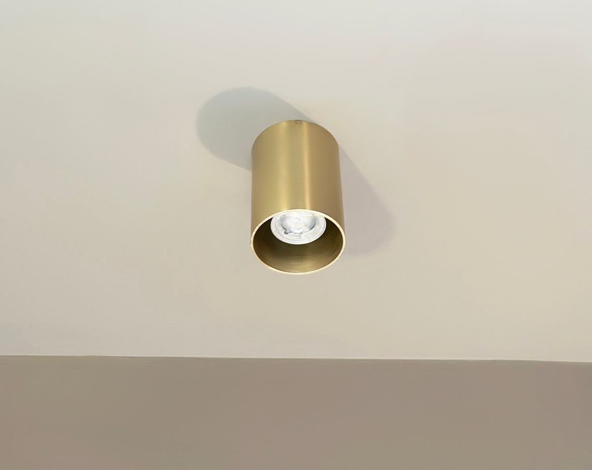 The Beau Laiton Trimless Downlight by Long Made Co. is a gold minimalist brass fixture mounted on a white ceiling, casting a subtle shadow behind it.