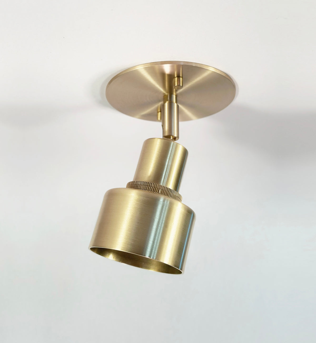 The Troon Spot by Long Made Co. is a modern brass ceiling light featuring an adjustable cylindrical shade on a round base, offering stylish directional downlighting for any white ceiling.