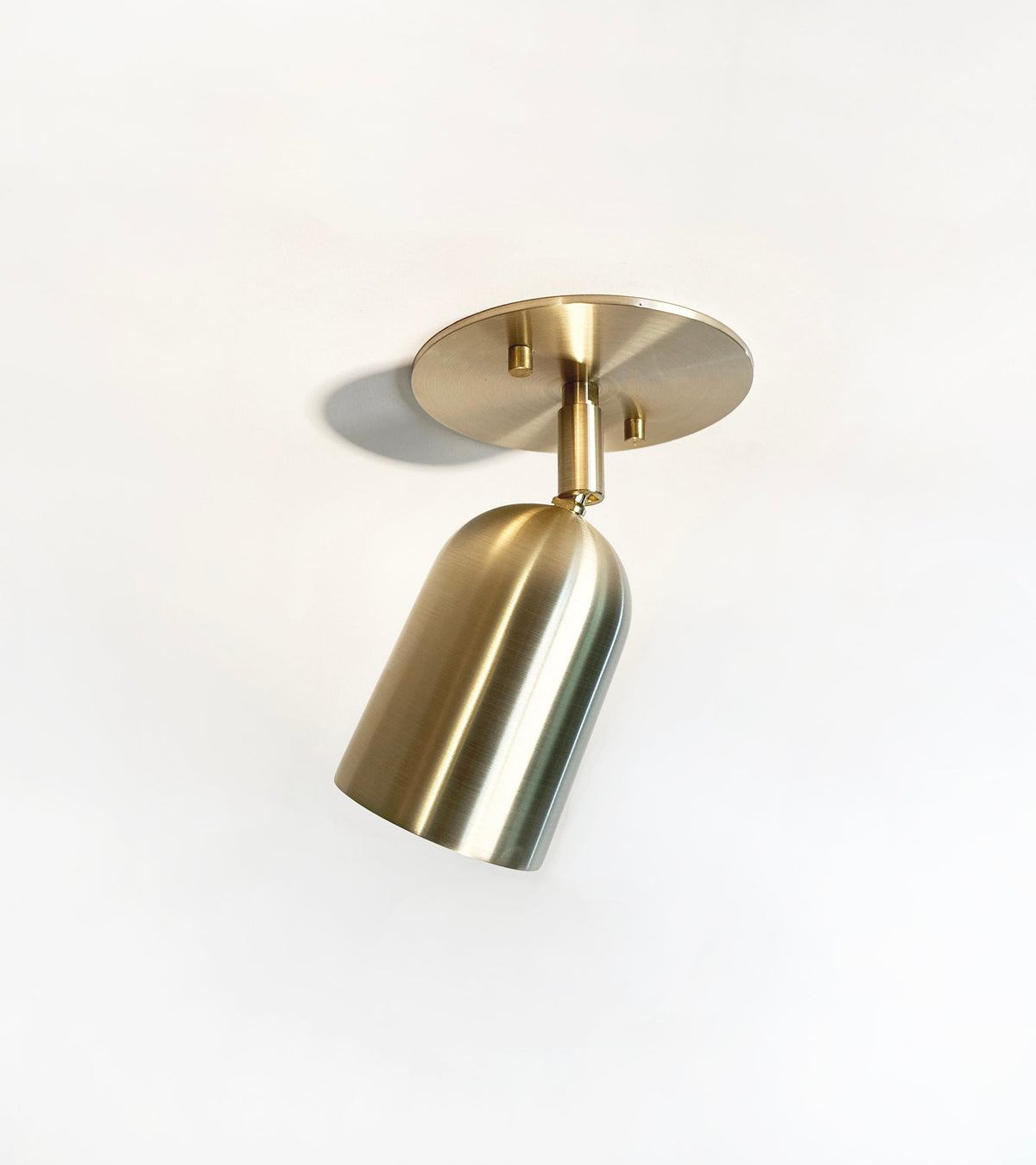 The Campana Adjustable Spot by Long Made Co. is a modern solid brass spotlight with a cylindrical, downward-facing shade on a round base, providing stylish directional ceiling lighting against a plain white background.