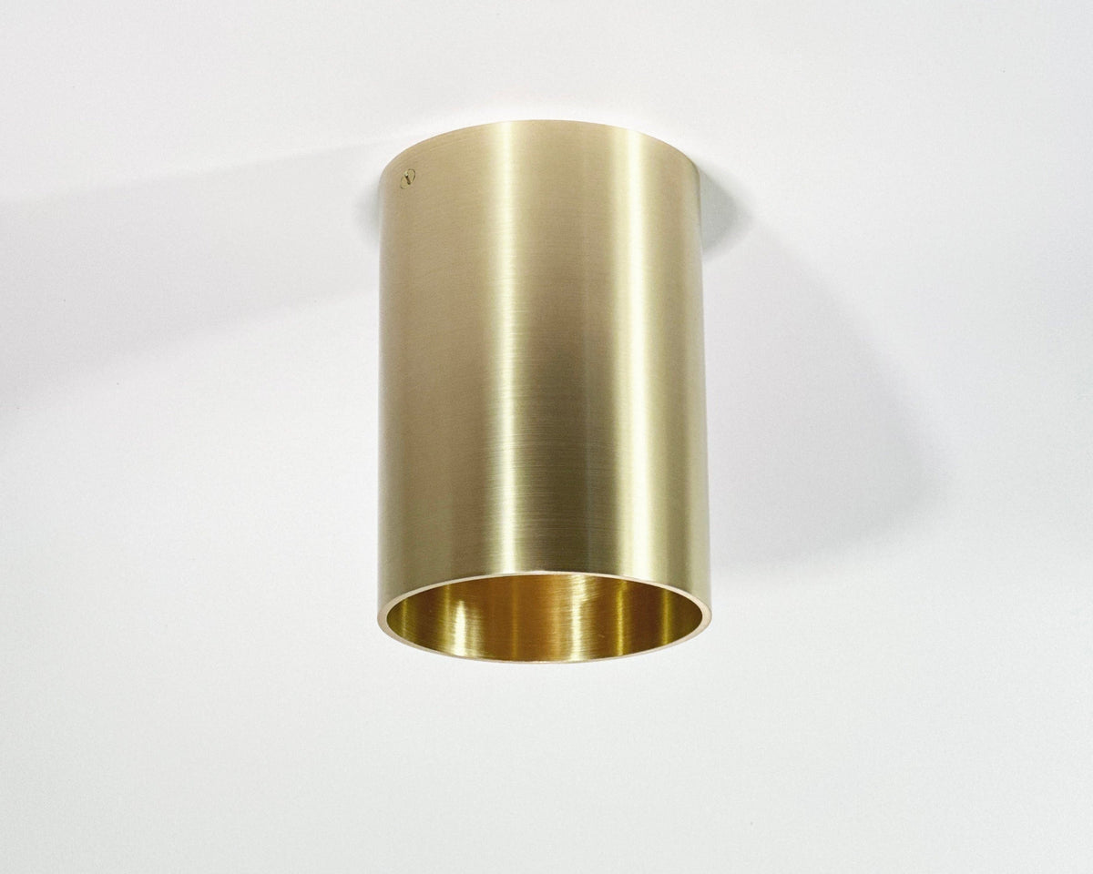 A cylindrical brass downlight fixture with a fixed drum shade head in a down position, showing a sleek metallic finish.