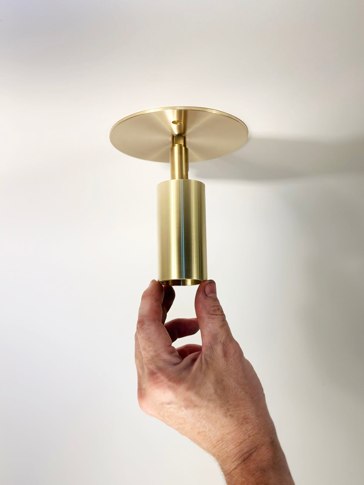 A hand adjusts the Long Made Co. Micro Adjustable Spot, a modern gold ceiling light with an ultra-thick inset cylinder head, against a white ceiling—ideal for minimalist monopoint lighting setups.