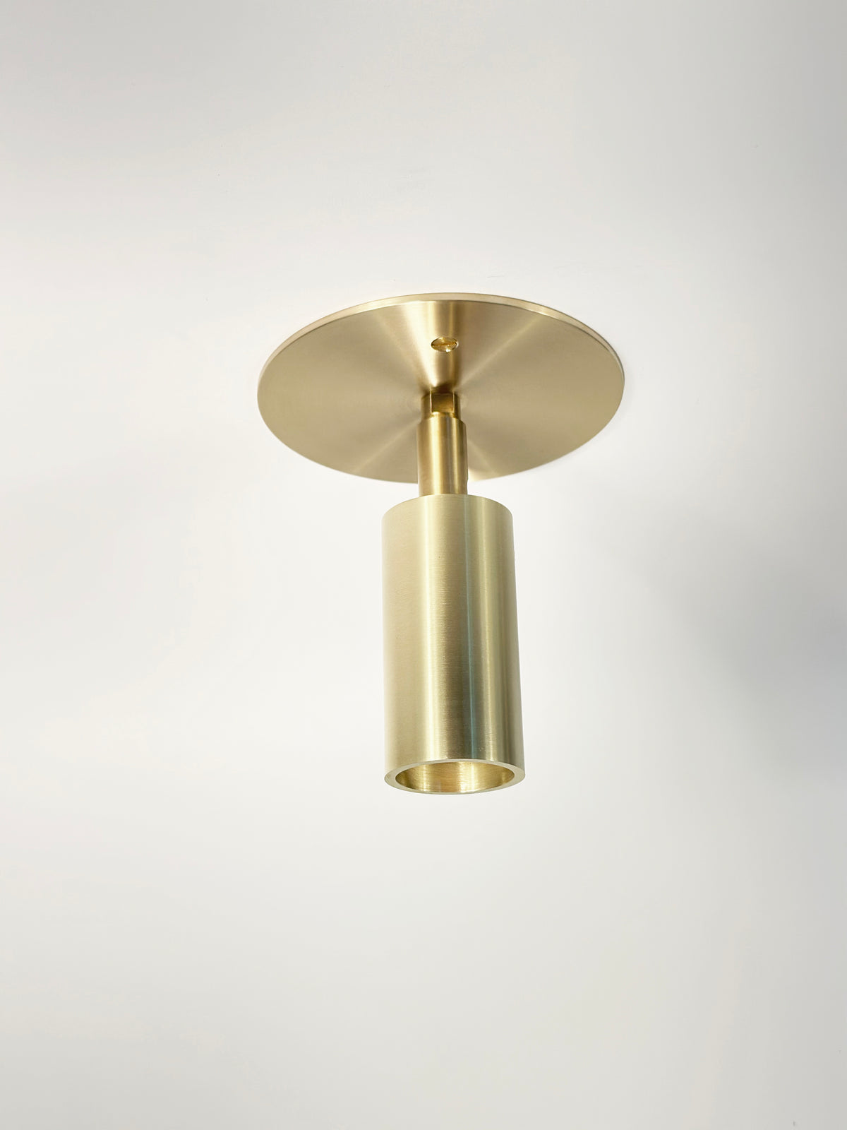 The Micro Adjustable Spot by Long Made Co. features a round base and an ultra-thick inset cylinder head, offering striking minimalist monopoint brass lighting on a plain white ceiling.