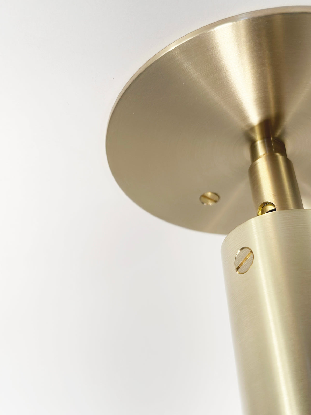 Close-up of the Micro Adjustable Spot by Long Made Co.—a brushed brass ceiling fixture from their Micro Spot Series, featuring an ultra-thick inset cylinder head and a round base with metallic screws, mounted on a white ceiling.