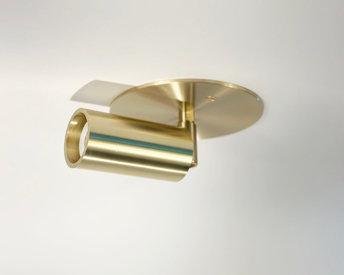 The Micro Adjustable Spot by Long Made Co. is a modern gold cylindrical spotlight from the Micro Spot Series, featuring an ultra-thick inset cylinder head and mounted on a round ceiling plate for a sleek, minimalist look against a white background.