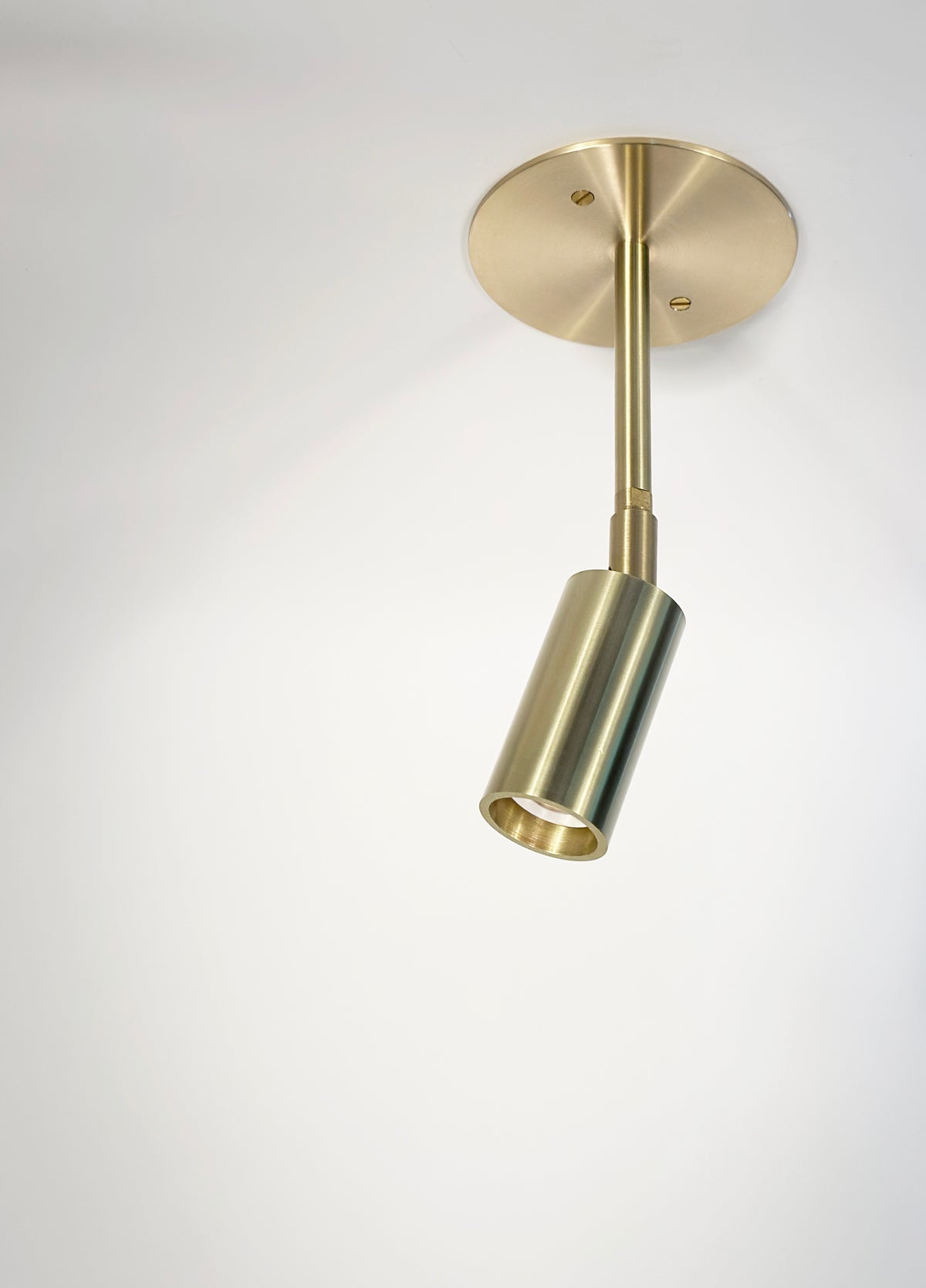 The Micro Drop Spot by Long Made Co. is a single brass-colored cylindrical ceiling light, mounted on a white ceiling and angled downward—a minimalist fixture with premium alternative lighting appeal.