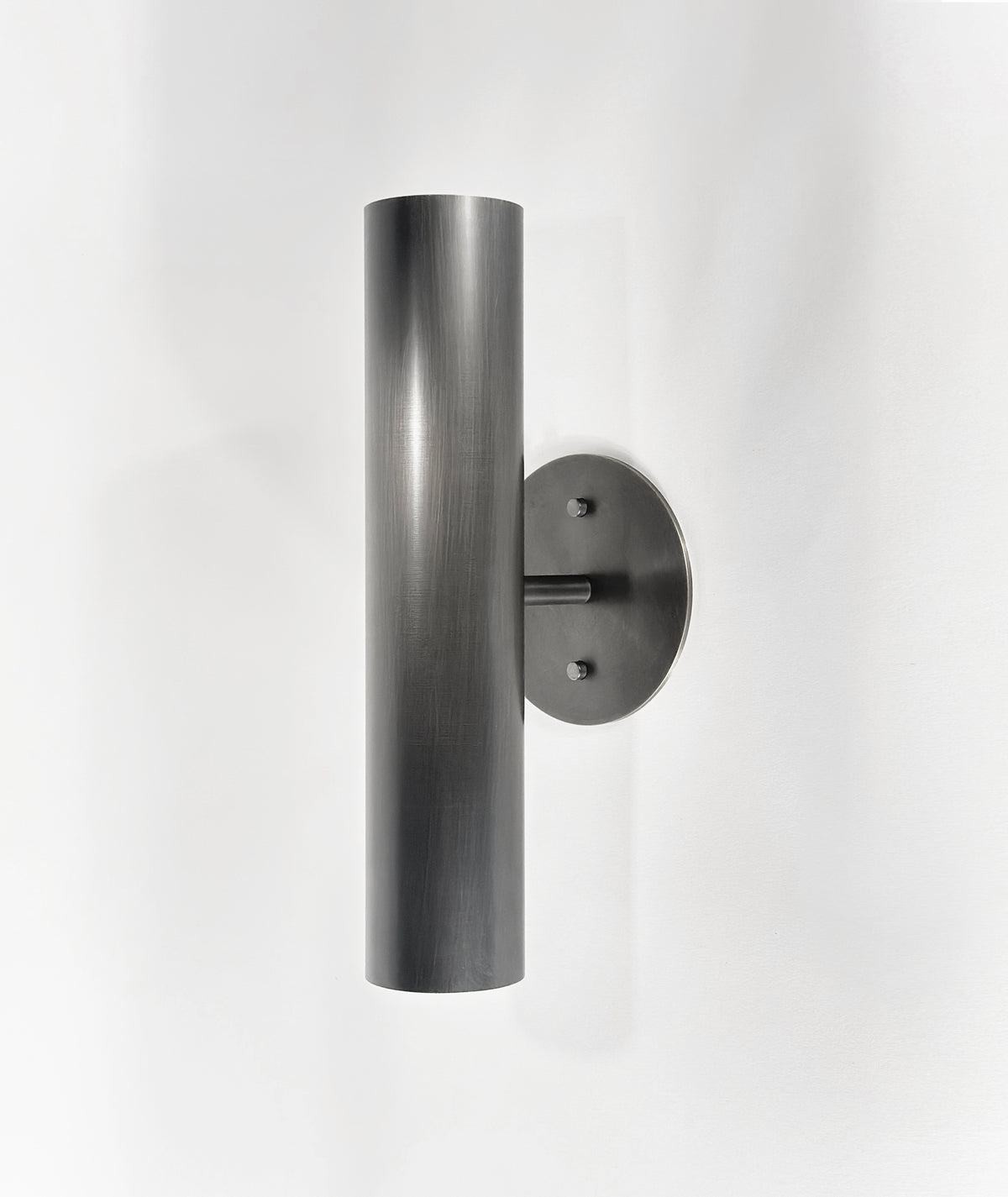 The Brass Cylinder Up-Down Sconce by Long Made Co. features a modern cylindrical brass design with a round base, shown mounted on a white wall—ideal for fans of mid-century modern lighting.