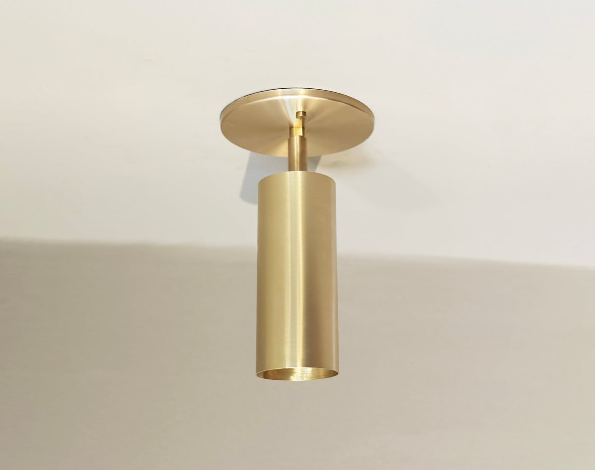 The Brass Cylinder Adjustable Spot - Top Mount w/ Long Shade by Long Made Co. is a modern brass ceiling light that adds a mid-century modern touch and sleek style to your space while casting a subtle shadow from the white ceiling.