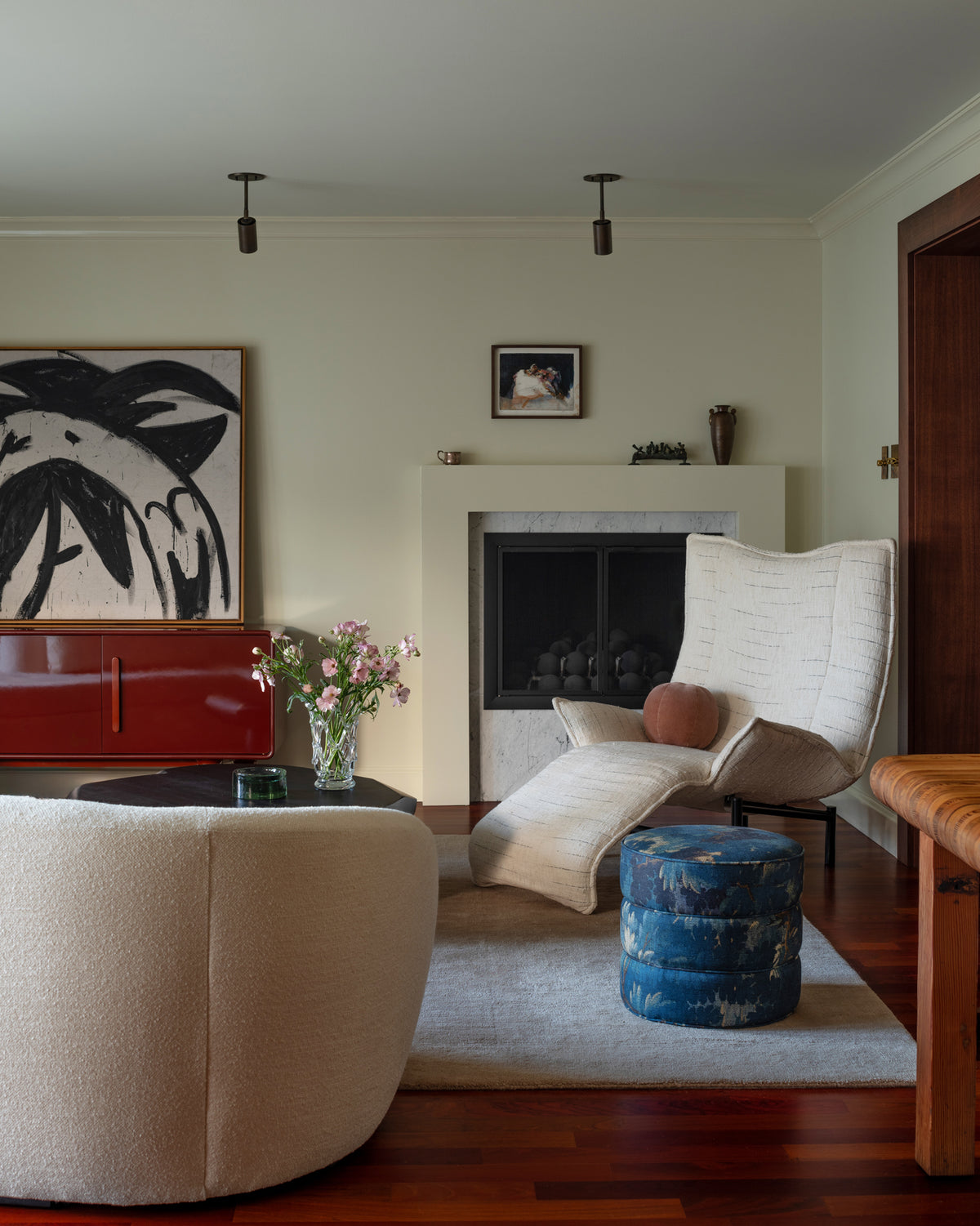 Living room with a white armchair, round ottoman, and artwork on the wall.