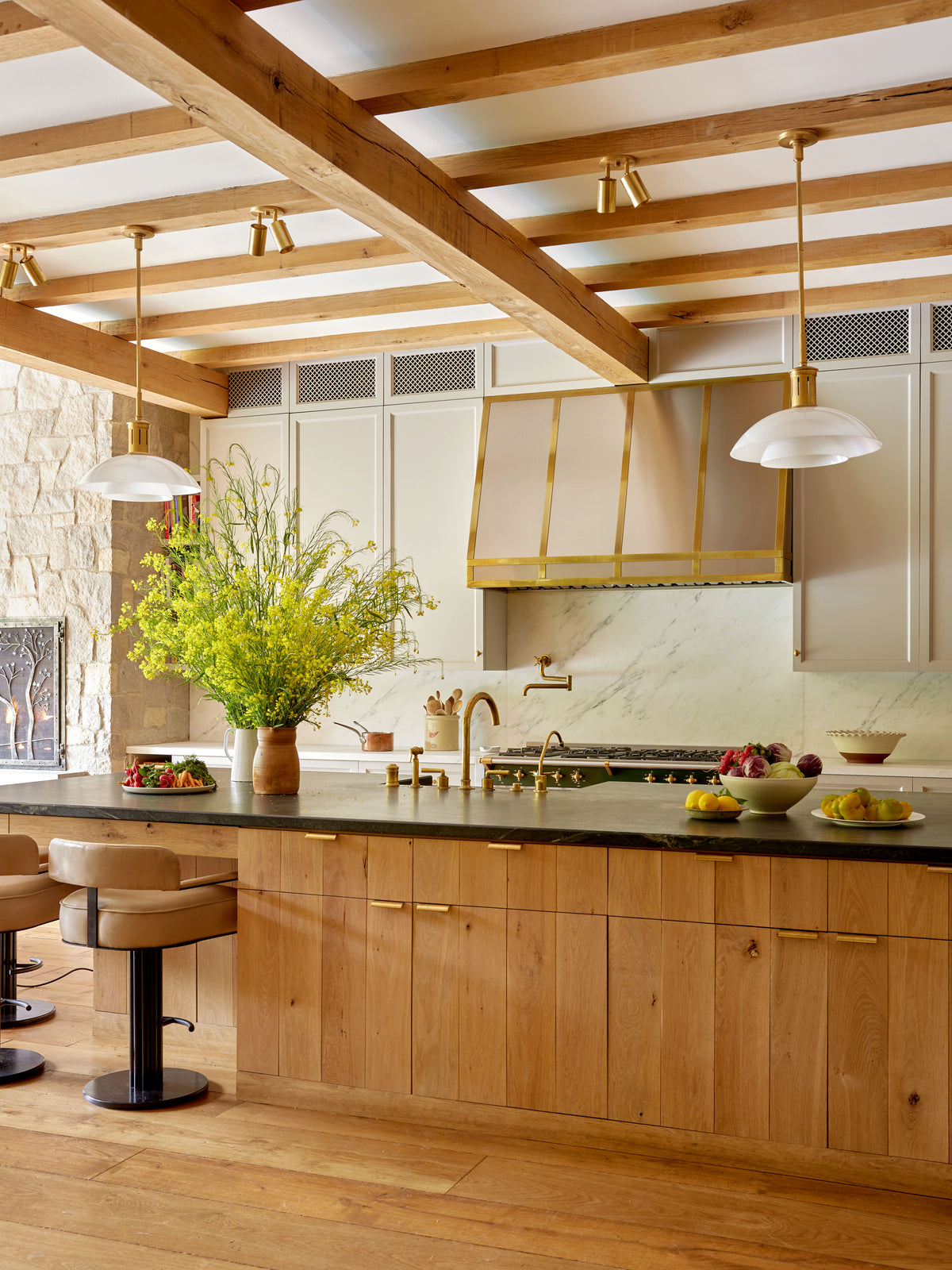 Sunny kitchen with wooden beams, light wood cabinets, a large island with tan stools, marble backsplash, and gold accents. Mid-century modern warmth is enhanced by Long Made Co.’s Brass Cylinder Double / Triple Spot lighting.