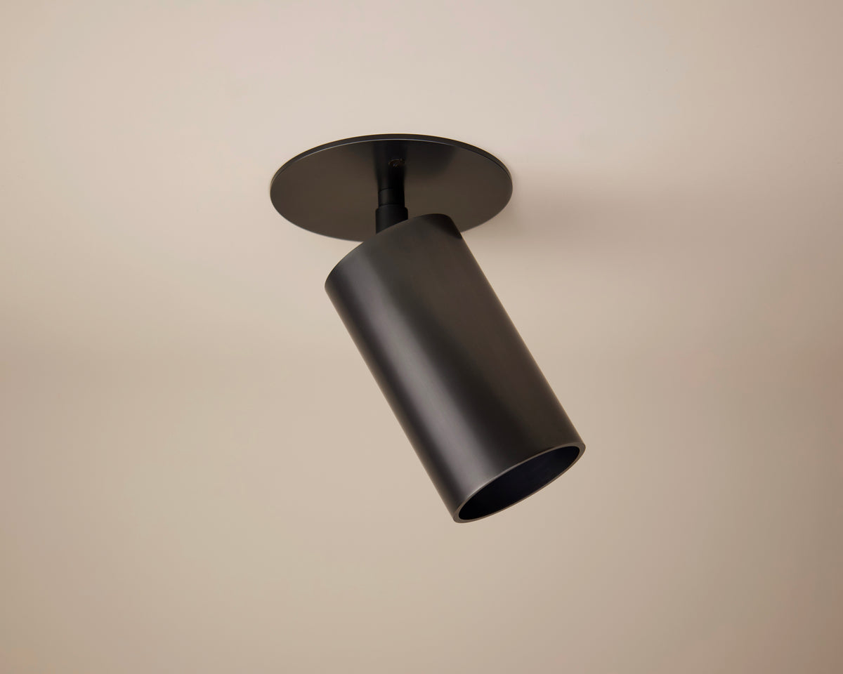 The Beau Laiton Monopoint by Long Made Co. is a modern black cylindrical ceiling spotlight, mounted on a beige ceiling and angled downward—an ideal addition to minimalist brass lighting schemes.