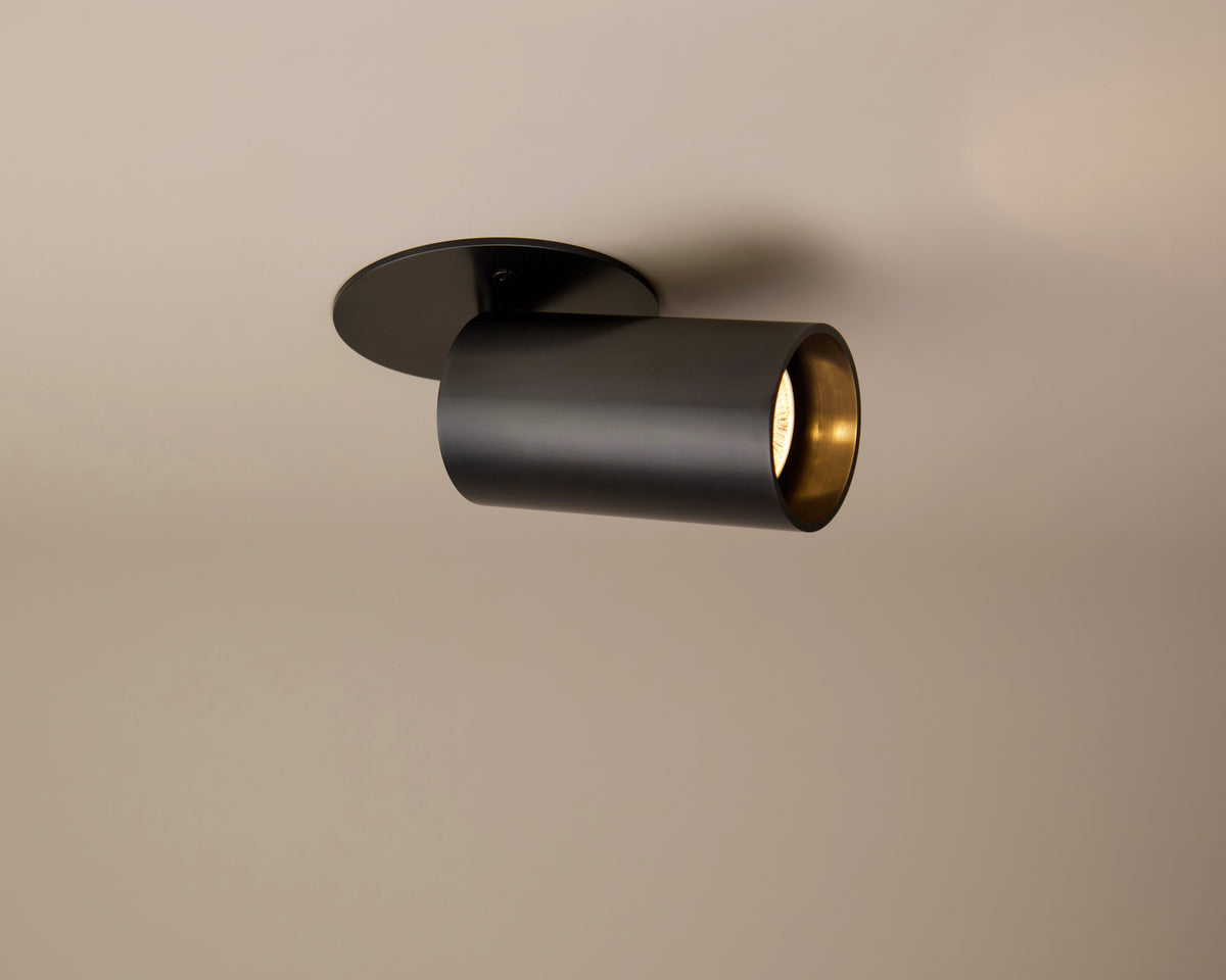 The Beau Laiton Monopoint by Long Made Co. is a black cylindrical ceiling spotlight with a metallic gold interior, mounted on a beige ceiling for modern minimalism and understated elegance in any space.