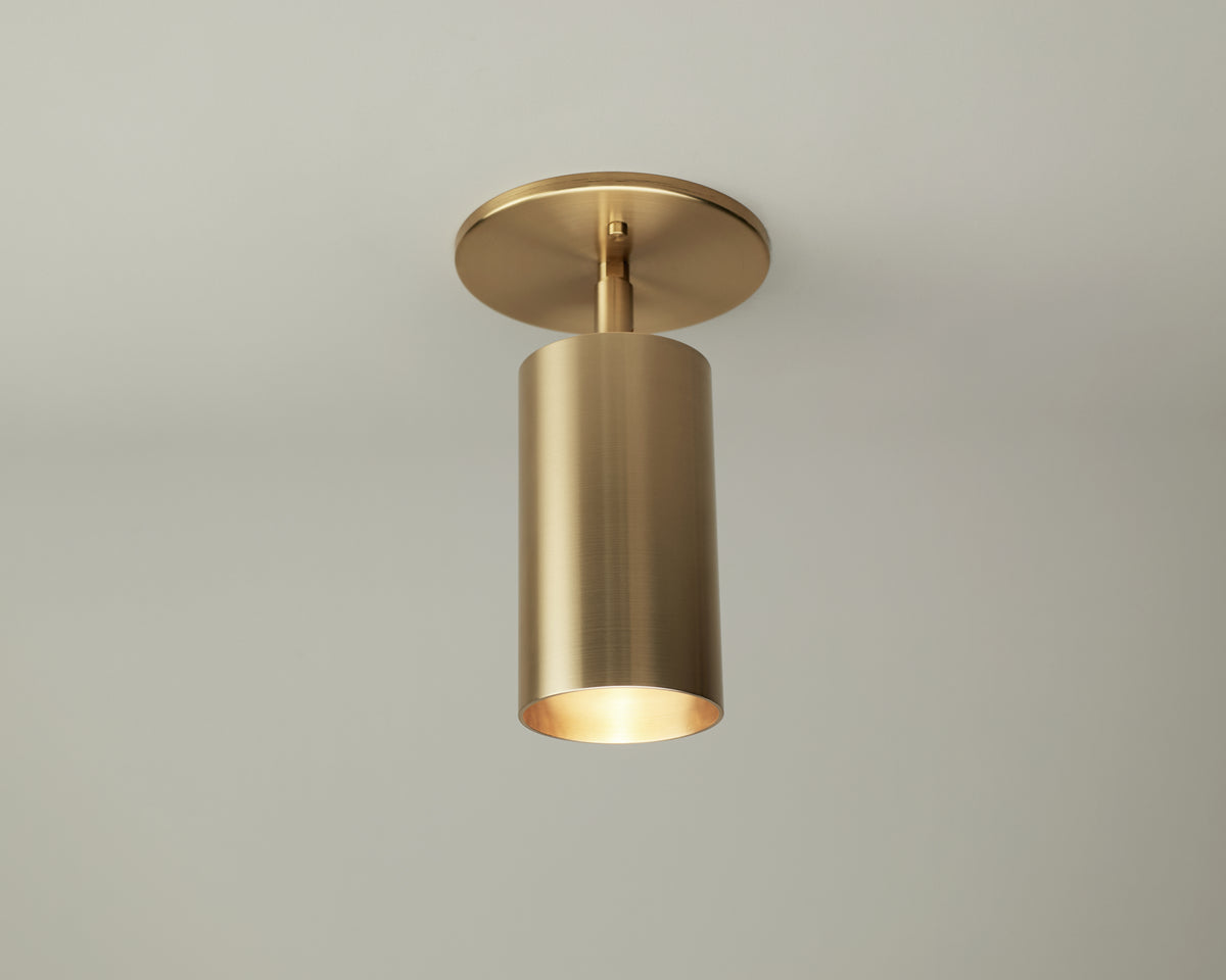 The Highland Adjustable Spot by Long Made Co. features a cylindrical brushed brass shade and round brass base, mounted on a white ceiling to cast soft downward light as part of the Highland Series lighting collection.