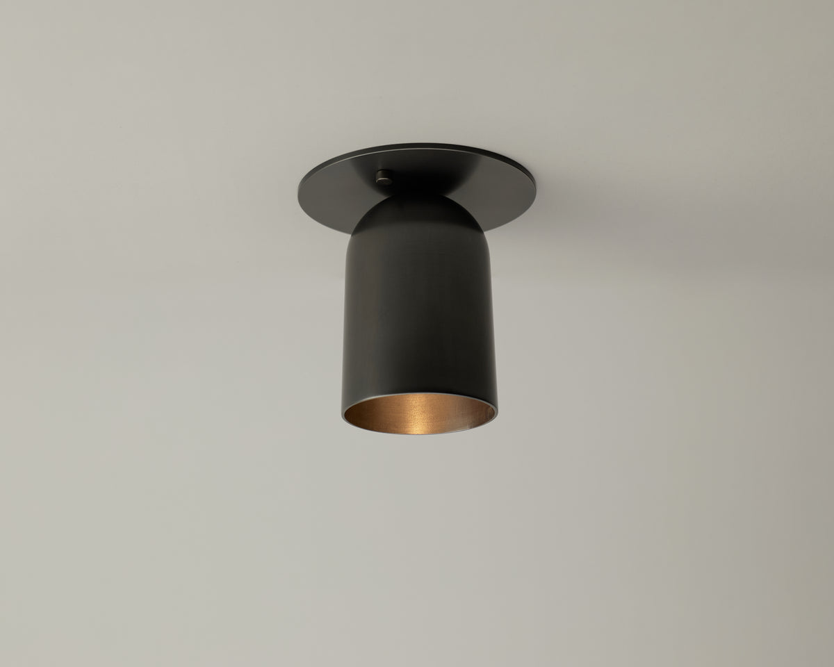 The Campana Flush Spot by Long Made Co., a black cylindrical flush mount ceiling downlight with a wide rim and handcrafted for a refined finish, is installed on a plain white ceiling.