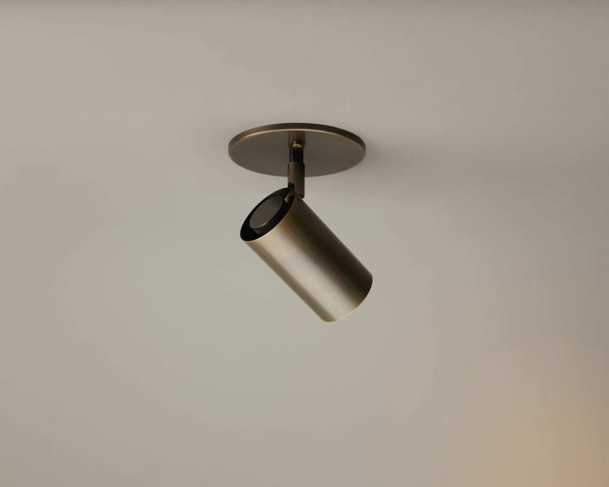 A modern, cylindrical Brass Cylinder Adjustable Spot - Side Mount by Long Made Co. is mounted on a round ceiling plate against a plain, light-colored ceiling. Inspired by mid-century modern lighting, this adjustable directional downlight brings both style and functionality to any contemporary space.