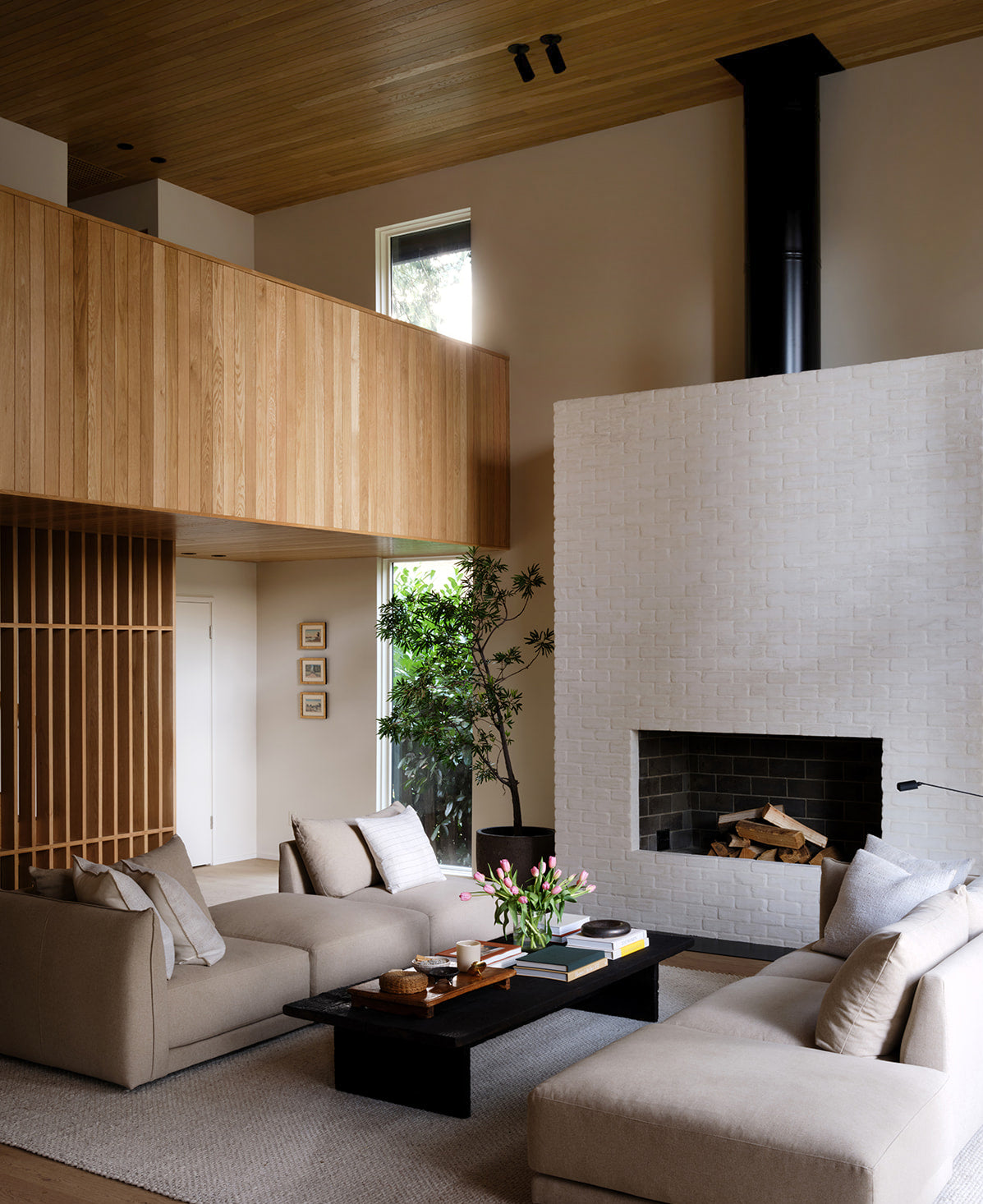 A modern living room with beige sofas, a black coffee table, wood accents, large windows, and minimalist spotlights from the Long Made Co. Cove Adjustable Spot series brightening the space.