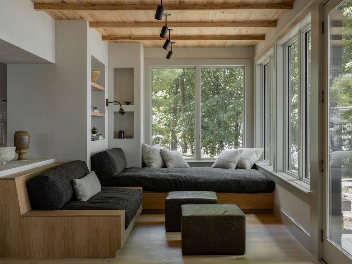 A cozy, modern living space with wood ceiling beams, a dark gray sectional sofa, and a built-in daybed—illuminated by Long Made Co.'s Cove Drop Spot minimalist spotlights for an inviting atmosphere.
