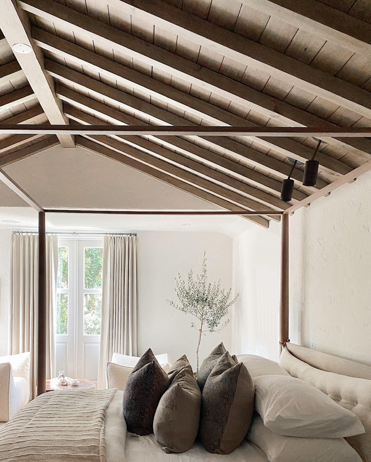 Neatly made bed with decorative pillows in a bedroom with wooden beams on the ceiling with Cove Drop Spots on ceiling.