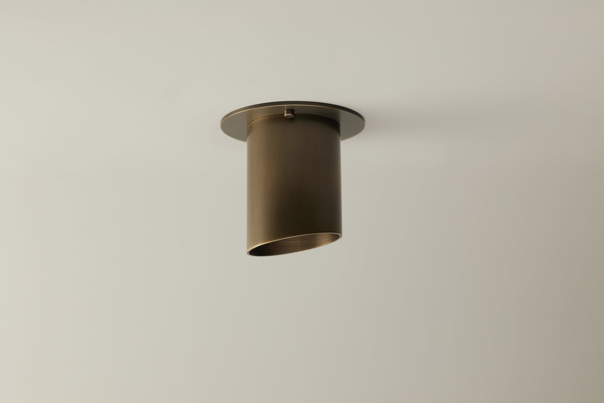 The Highland Angle Spot - Stocky by Long Made Co. is a handmade, modern brass cylinder light with an angled edge and open bottom, mounted flush on a white ceiling for a sleek, minimalist look. Crafted in Texas.