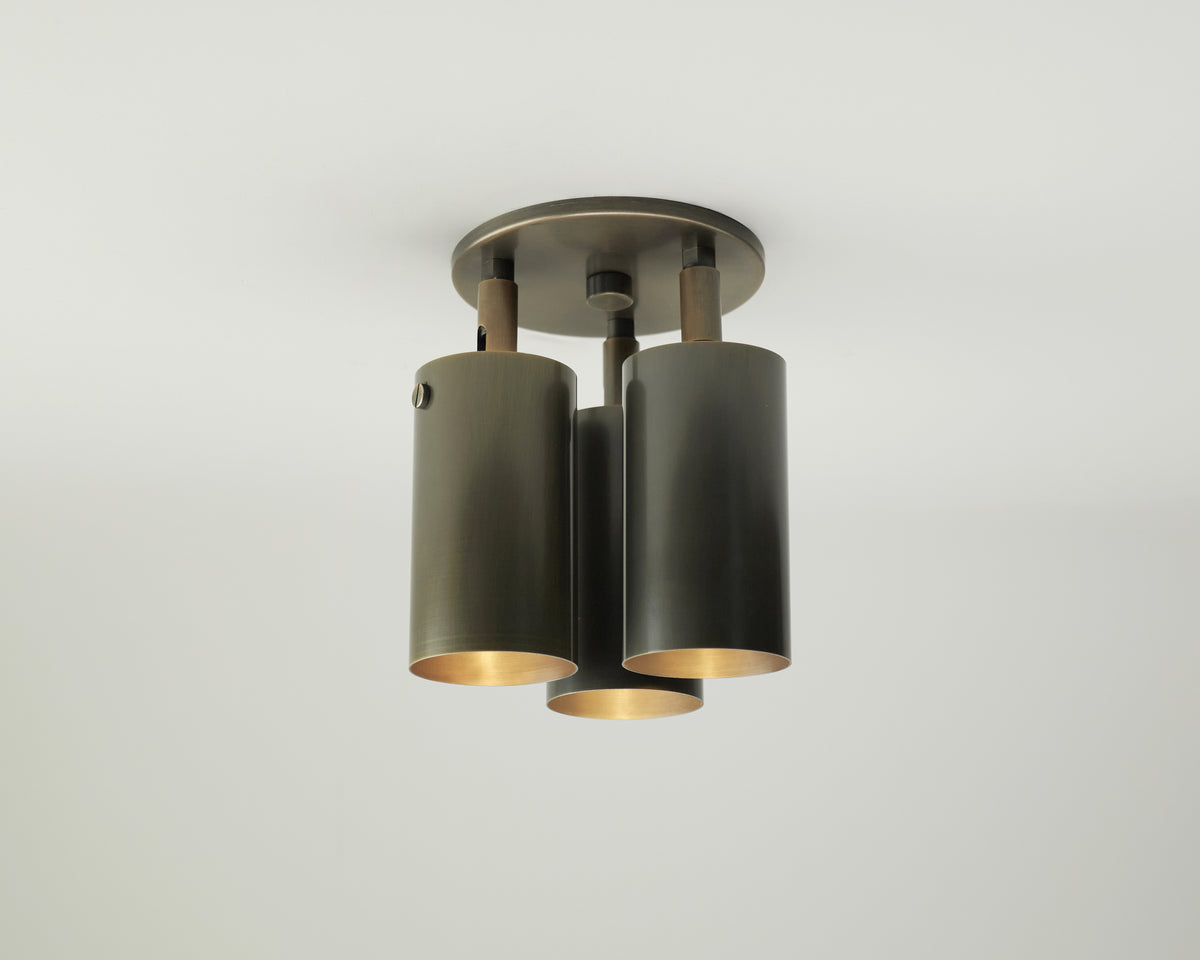 Introducing the Brass Cylinder Triple Spot by Long Made Co., a modern ceiling light fixture featuring three cylindrical, brushed metal shades elegantly suspended from a round base. Set against a minimalist, light-colored background, this piece echoes the timeless appeal of mid-century modern lighting. Its adjustable spot light design provides customizable illumination, making it ideal for contemporary interiors.