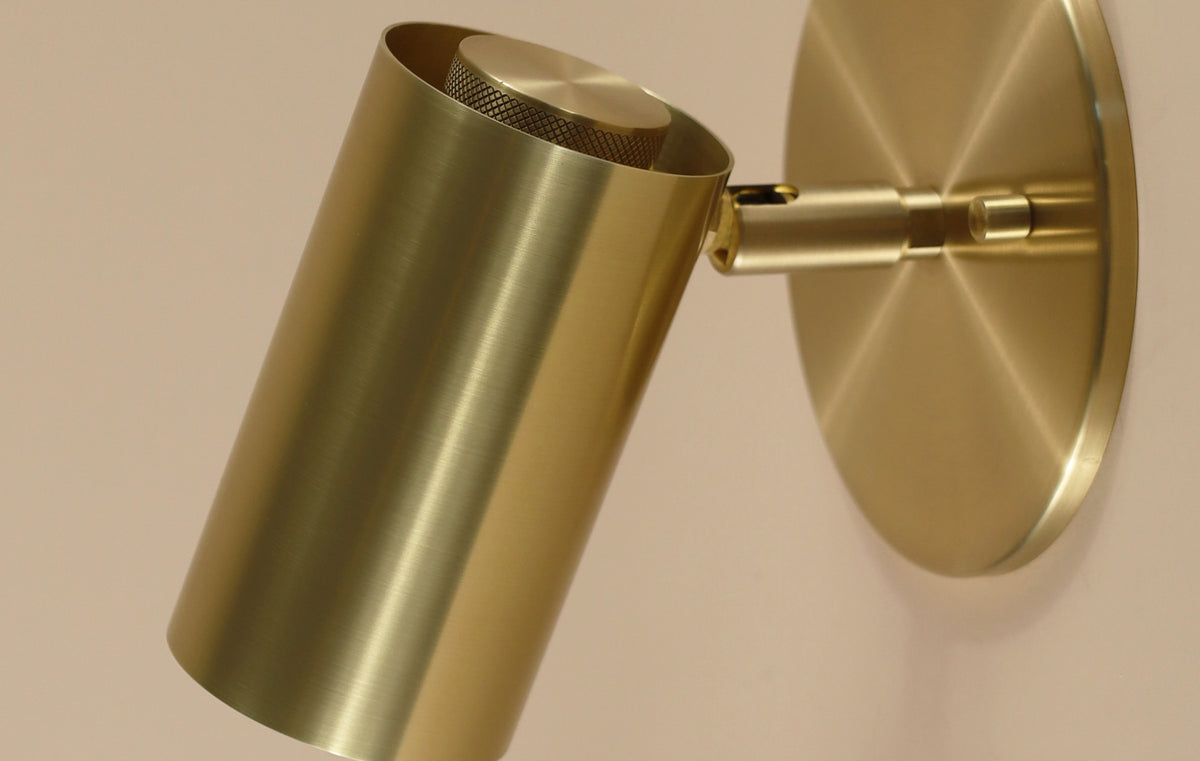 A close-up of the Brass Cylinder Wall Lamp by Long Made Co., featuring a modern cylindrical brass design with a brushed finish, mounted on a round base—an elegant, mid-century modern-inspired accent for any light-colored wall.