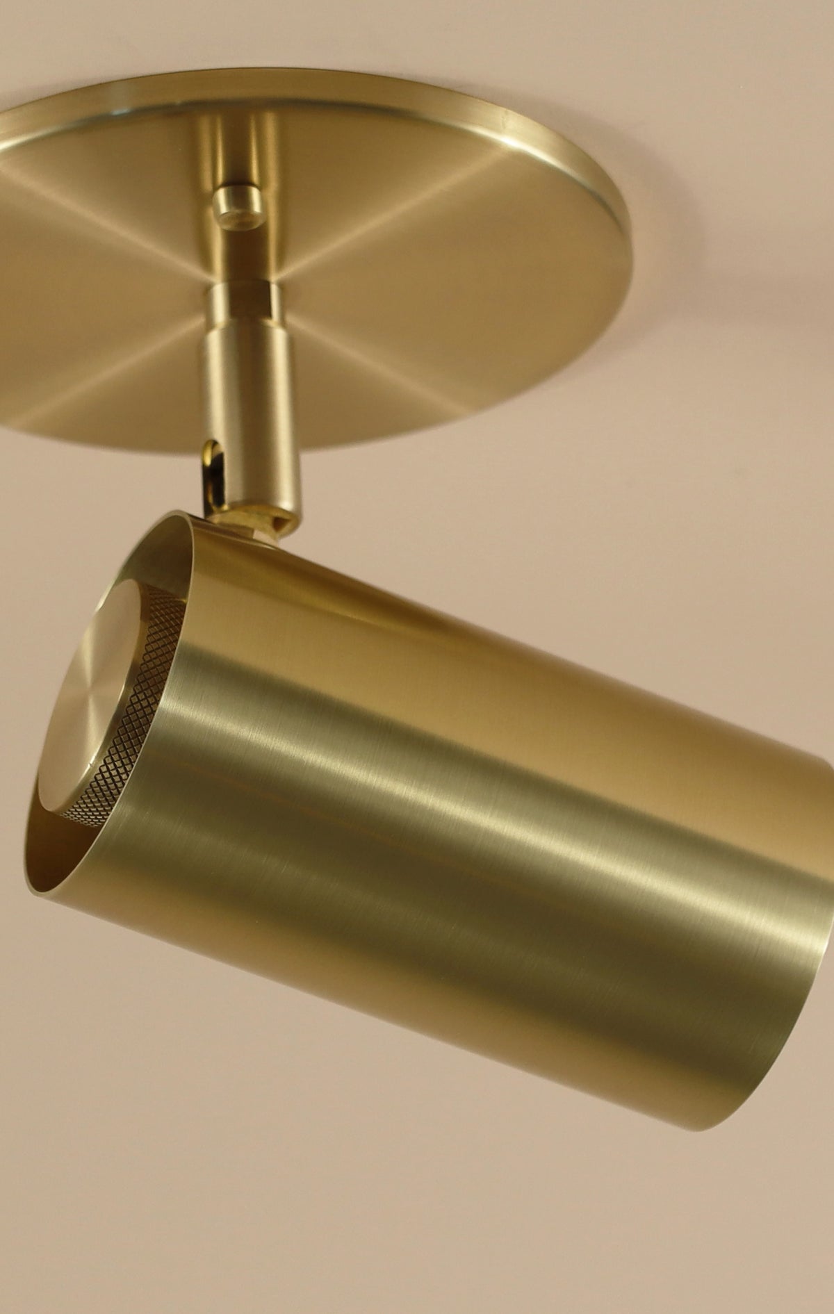 A close-up of the Brass Cylinder Adjustable Spot - Side Mount by Long Made Co. highlights its modern cylindrical design and circular base, shown mounted on a light-colored ceiling.