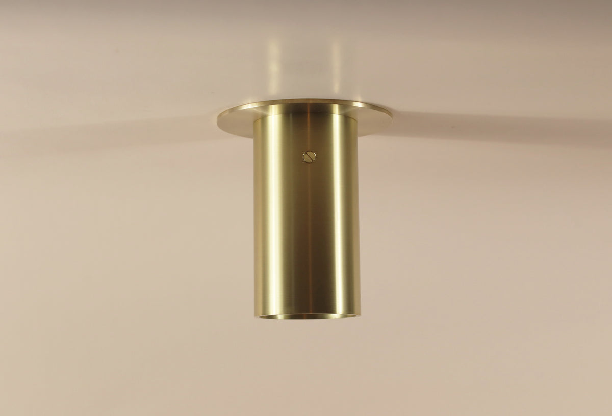 The Beau Laiton Flush Spot by Long Made Co. is a minimalist solid brass light with a brushed cylindrical design and flat circular base, seamlessly mounted on a plain, light-colored ceiling.