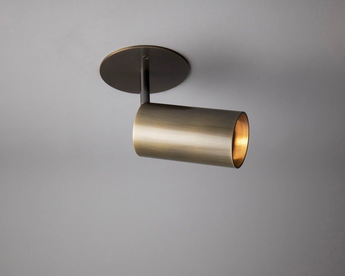 The Beau Laiton Drop Monopoint by Long Made Co. is a modern cylindrical brass ceiling light mounted on a round base, angled slightly downward against a neutral gray background.