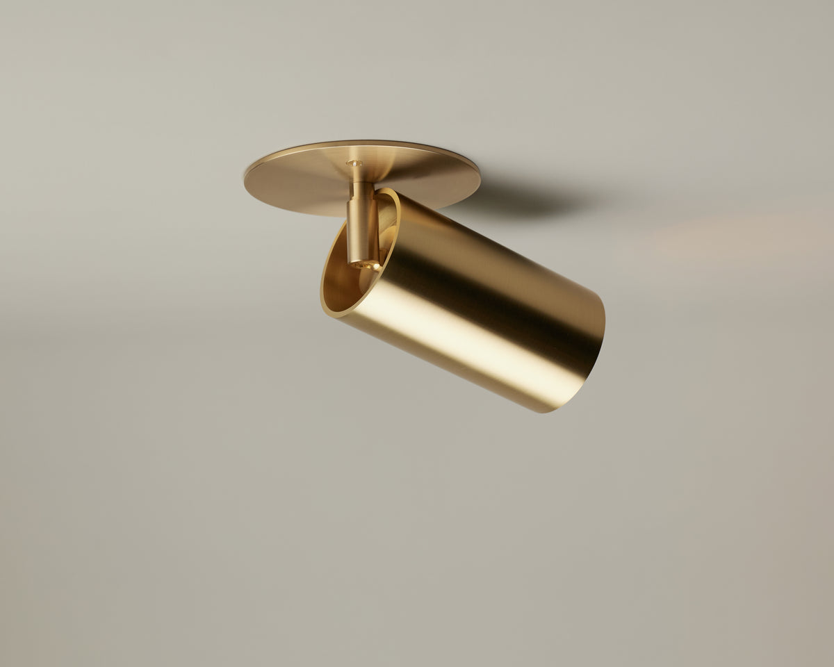 The Beau Laiton Monopoint by Long Made Co. is a modern gold cylindrical ceiling spotlight with a round base, mounted on a plain light-colored ceiling and angled downward. This premium fixture seamlessly combines minimalist brass lighting design with contemporary elegance.