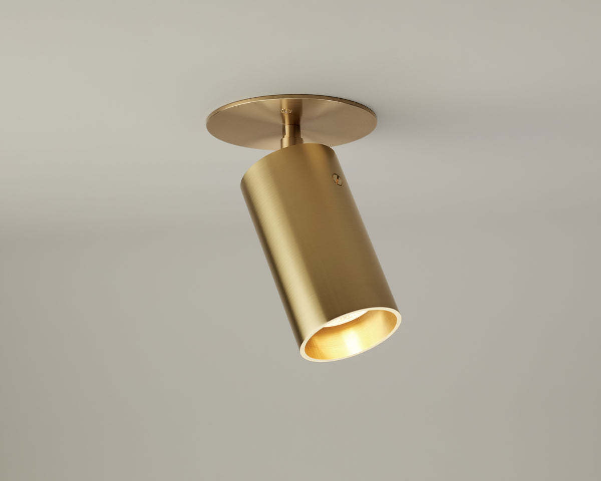 The Beau Laiton Monopoint by Long Made Co. is a premium, gold-colored cylindrical ceiling spotlight fixture mounted on a round base, angled downward and shown illuminated against a plain light gray background.
