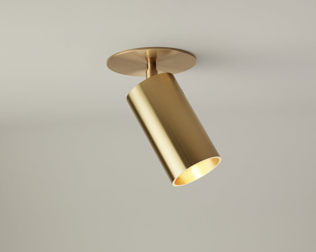 The Beau Laiton Monopoint by Long Made Co. is a premium gold cylindrical ceiling spotlight, mounted on a circular base and angled downward against a plain light-colored ceiling, providing minimalist brass lighting to any space.
