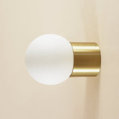Wall-mounted light fixture with gold finish and white glass shade on a beige background