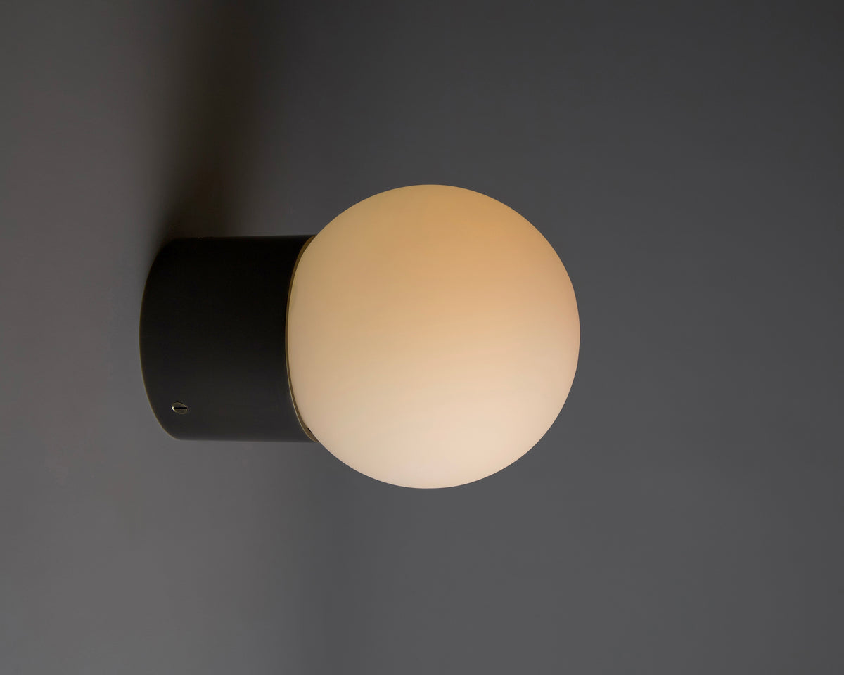 The Beau Laiton Trimless Sphere by Long Made Co. features a matte black cylindrical base and frosted white globe, casting a soft, warm glow—an elegant, minimalist sconce perfect for subtle sophistication in any space.