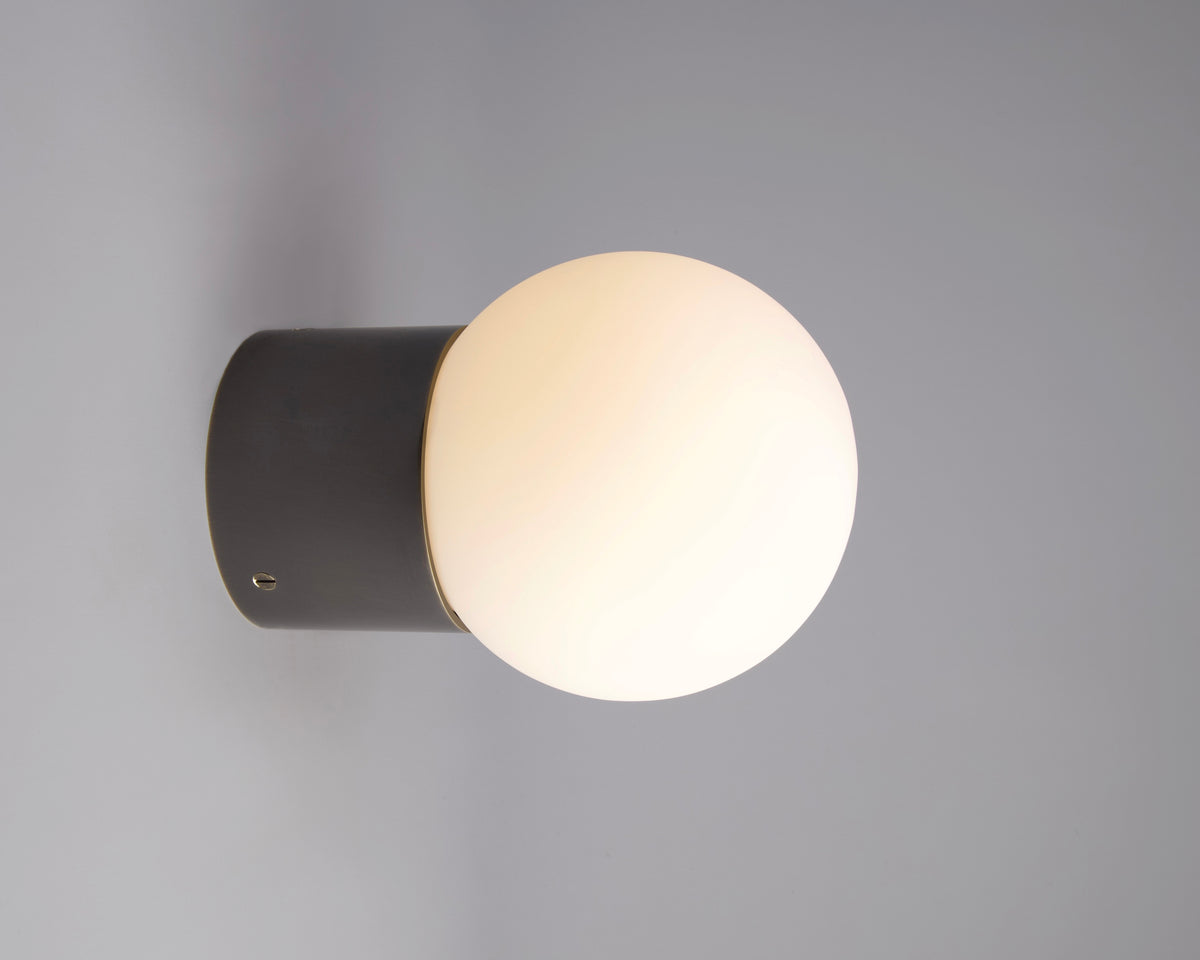 The Beau Laiton Trimless Sphere by Long Made Co. is a modern minimalist wall sconce with a round frosted white glass globe and dark cylindrical base—an elegant solid brass lighting choice for contemporary interiors.