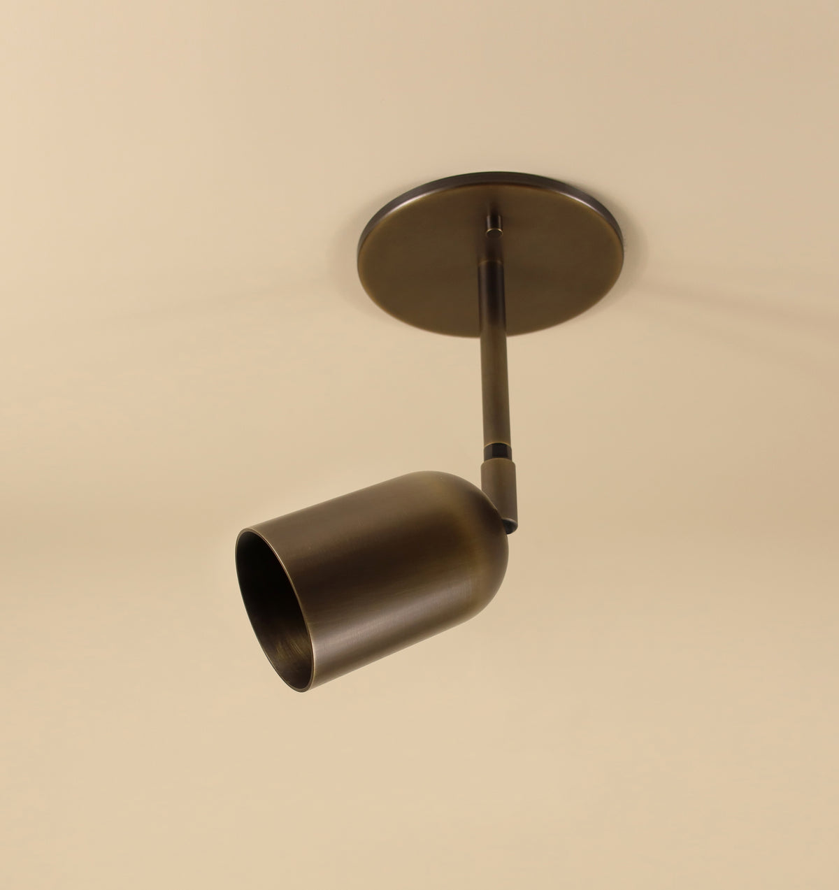 The Campana Drop Spot by Long Made Co., a sleek modern cylindrical brass ceiling downlight, is mounted on a round base against a plain beige ceiling.