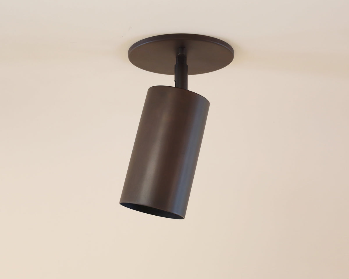 The Cove Adjustable Spot by Long Made Co. is a modern, cylindrical black solid steel downlight mounted on a white ceiling and angled downward.