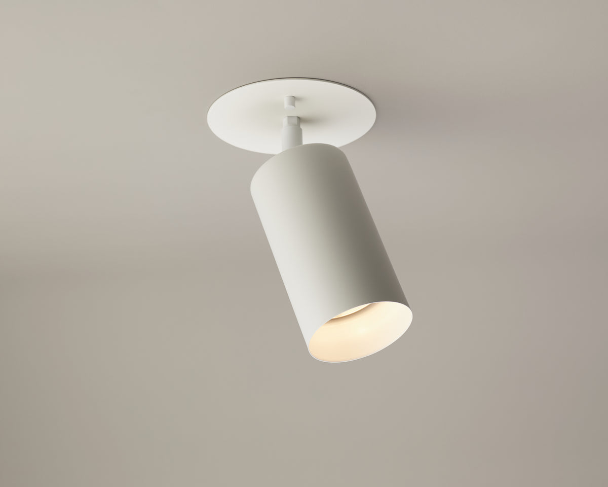 The Long Made Co. Cove Adjustable Spot is a modern white cylindrical ceiling spotlight crafted from solid steel, featuring a slightly angled beam and mounted on a round base, offering an elegant minimalist lighting solution for plain, light-colored ceilings.