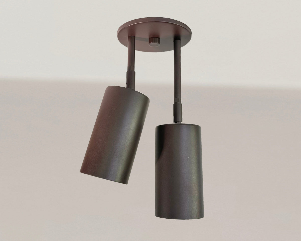 The Cove Double Drop Spot by Long Made Co. is a modern black ceiling fixture with two adjustable cylindrical steel spotlights, mounted on a white ceiling.