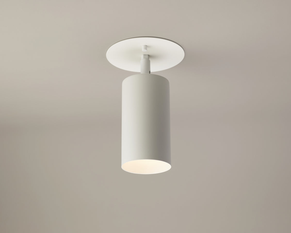 The Cove Adjustable Spot by Long Made Co. is a modern, cylindrical ceiling light fixture with a matte white finish, mounted on a beige ceiling and casting soft downlight in true minimalist lighting style.
