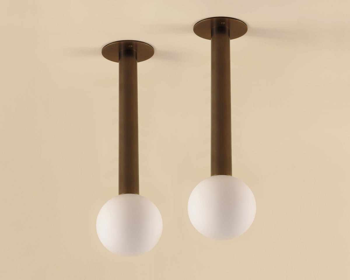 Two ceiling lights with brass fixtures and white spherical shades on a beige background