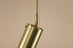 A close-up of the Brass Cylinder Drop Spot - Top Mount by Long Made Co., a modern cylindrical brass ceiling downlight fixture, hangs from a brass rod against a neutral beige background.